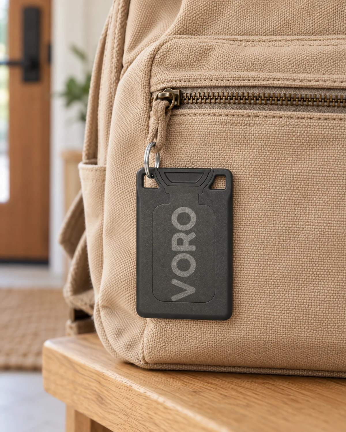 The charcoal VORO card attached through a corner slot to a canvas backpack zipper.